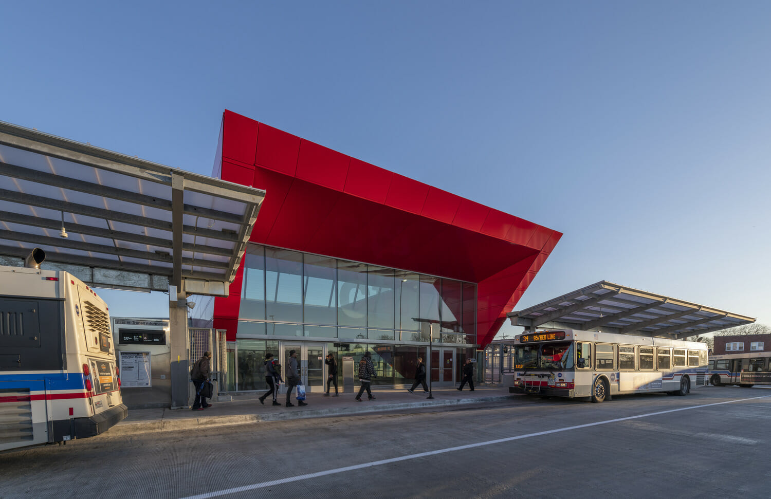 A red bus is parked in front of a red building.