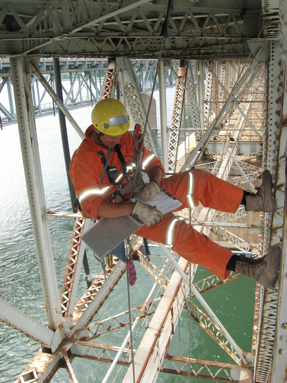 A man in orange is working on a bridge.