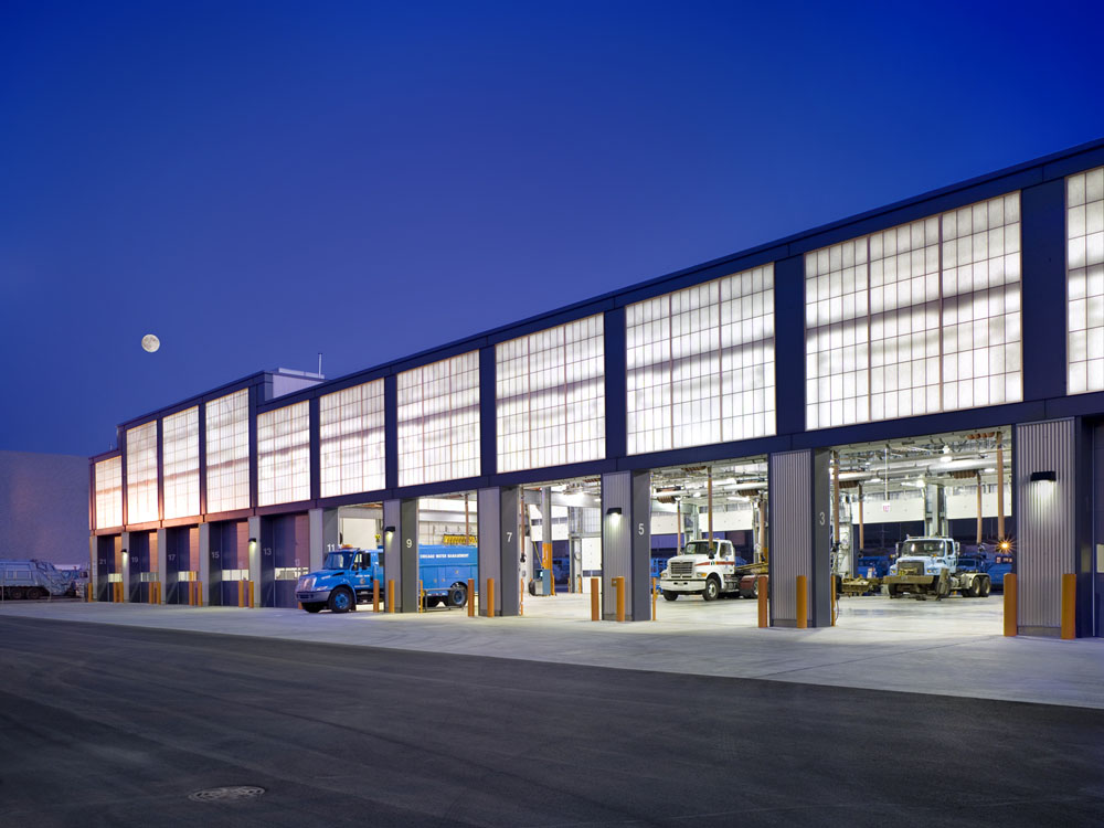 A large warehouse with trucks parked outside at night.