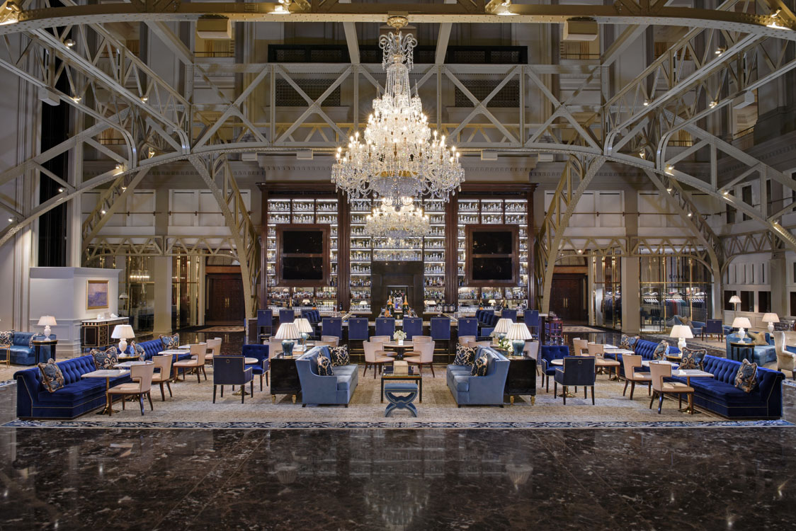 The lobby of a hotel with a chandelier and blue chairs.