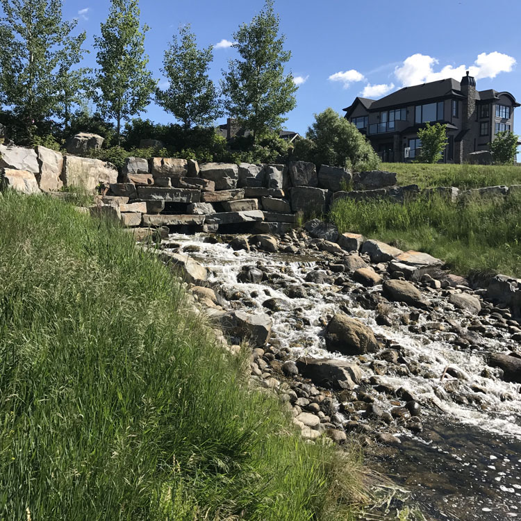 Un ruisseau avec des rochers et de l'herbe devant une maison.