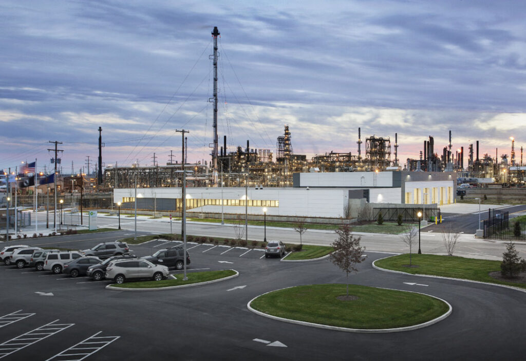 An oil refinery at dusk with cars parked in the parking lot.