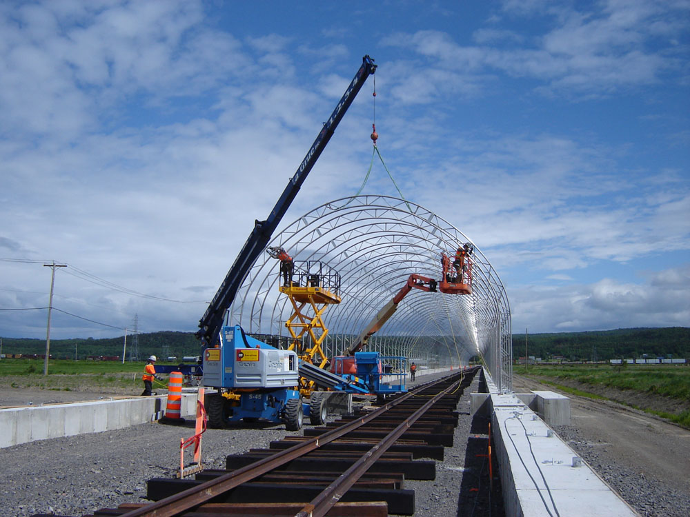 A crane is lifting a metal structure over a train track.