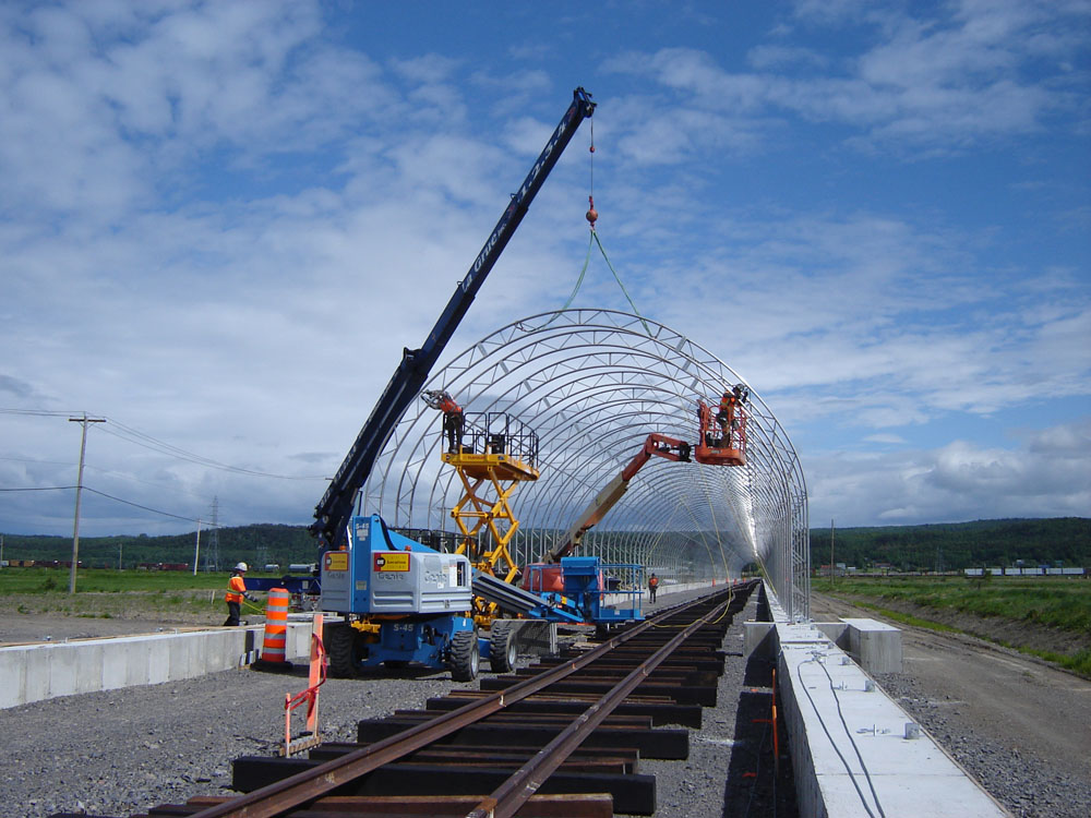 Une grue soulève une structure métallique au-dessus d'une voie ferrée.