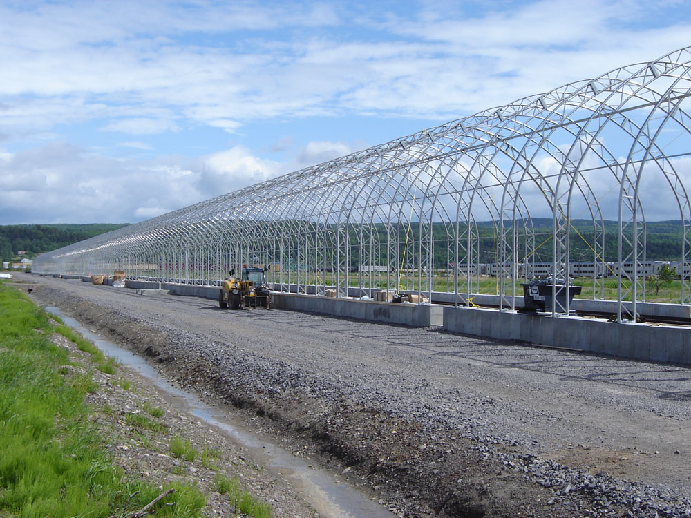 Une grande structure métallique sur une route à côté d’un champ.