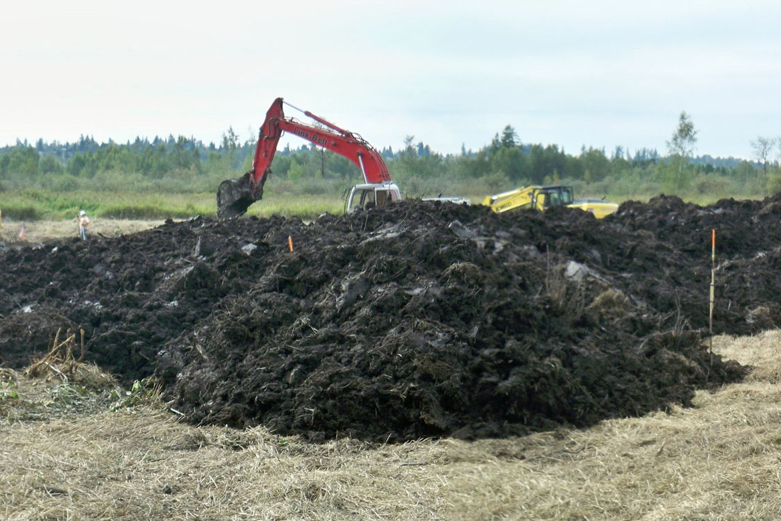 A pile of dirt in a field with an excavator.