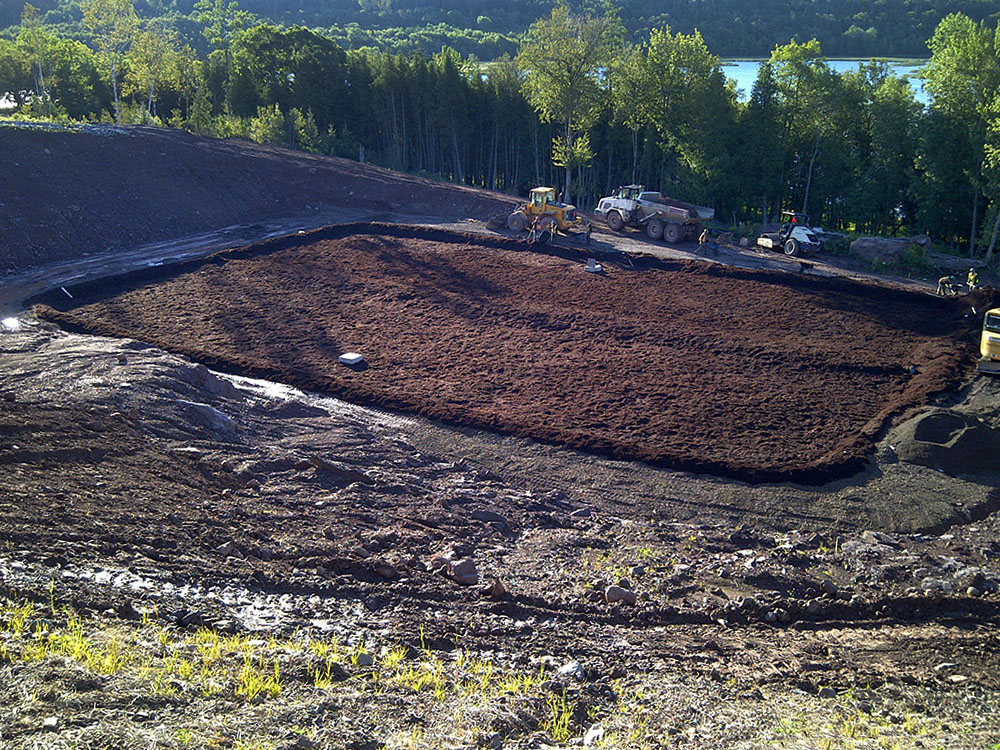 A large area of dirt is being dug up in the middle of a wooded area.