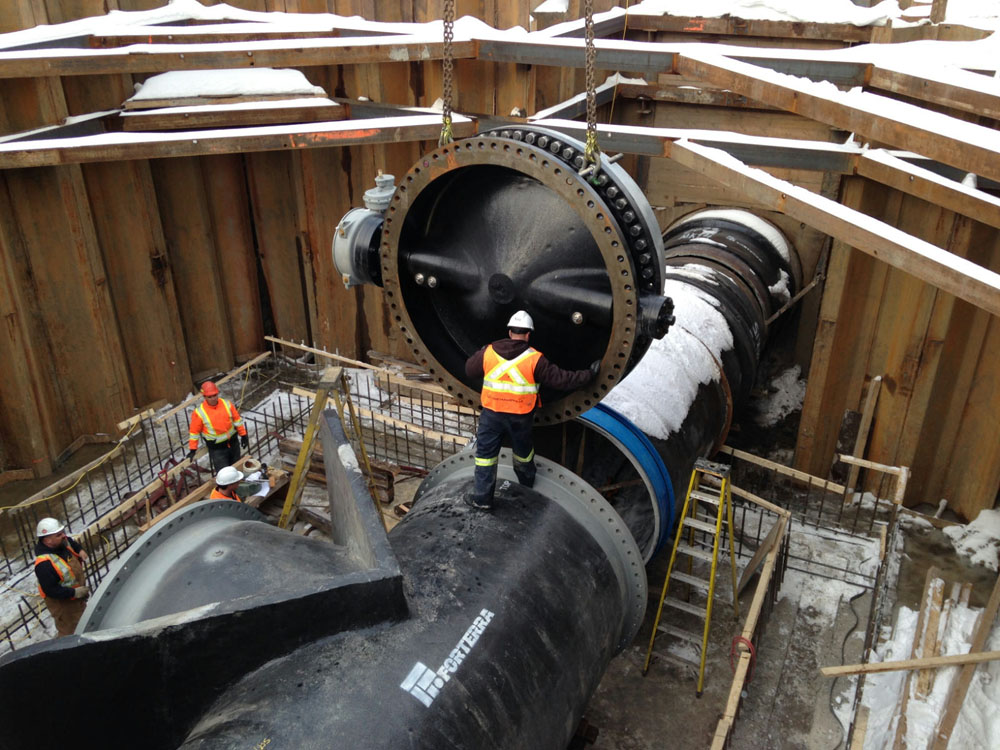 Workers working on a large pipe in a snowy area.