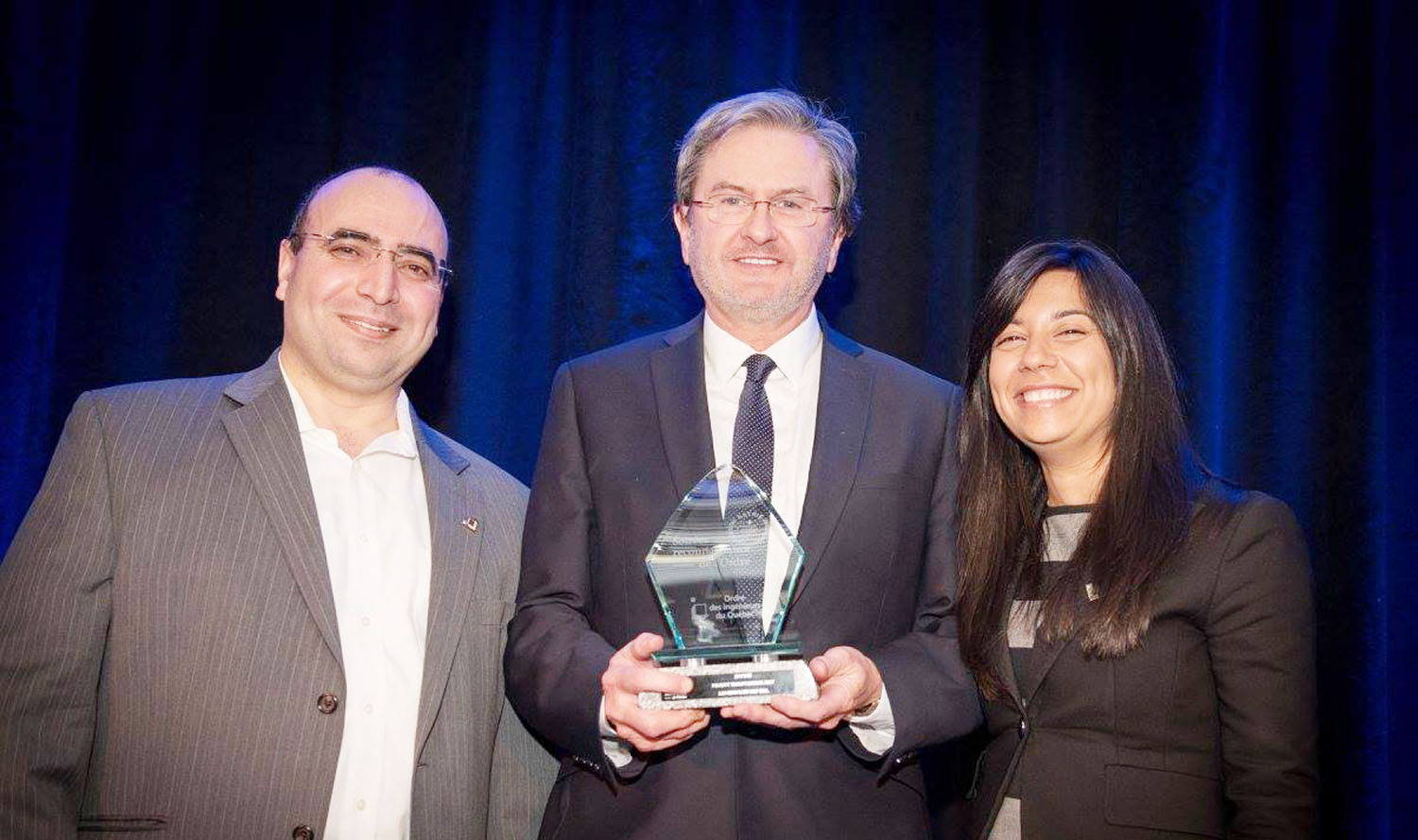 Three people standing next to each other holding an award.