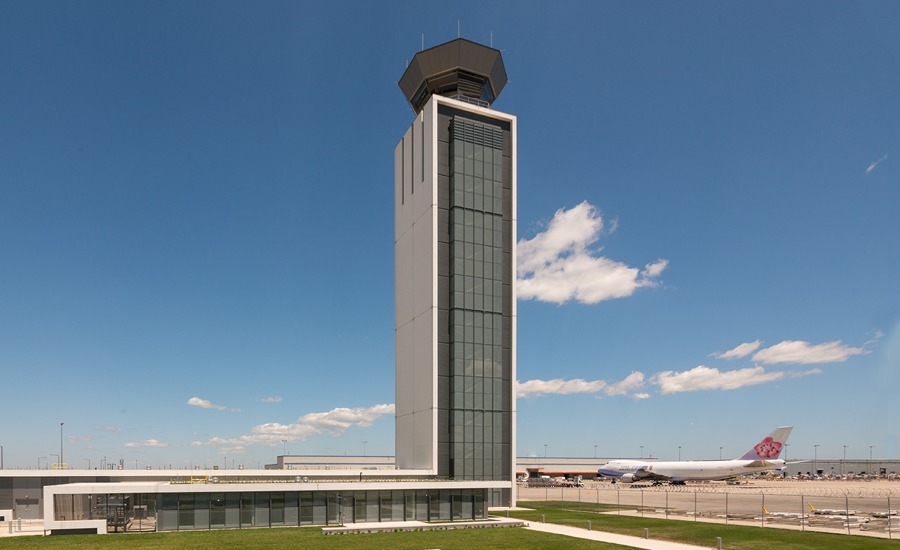 An airport control tower in front of a grassy field.