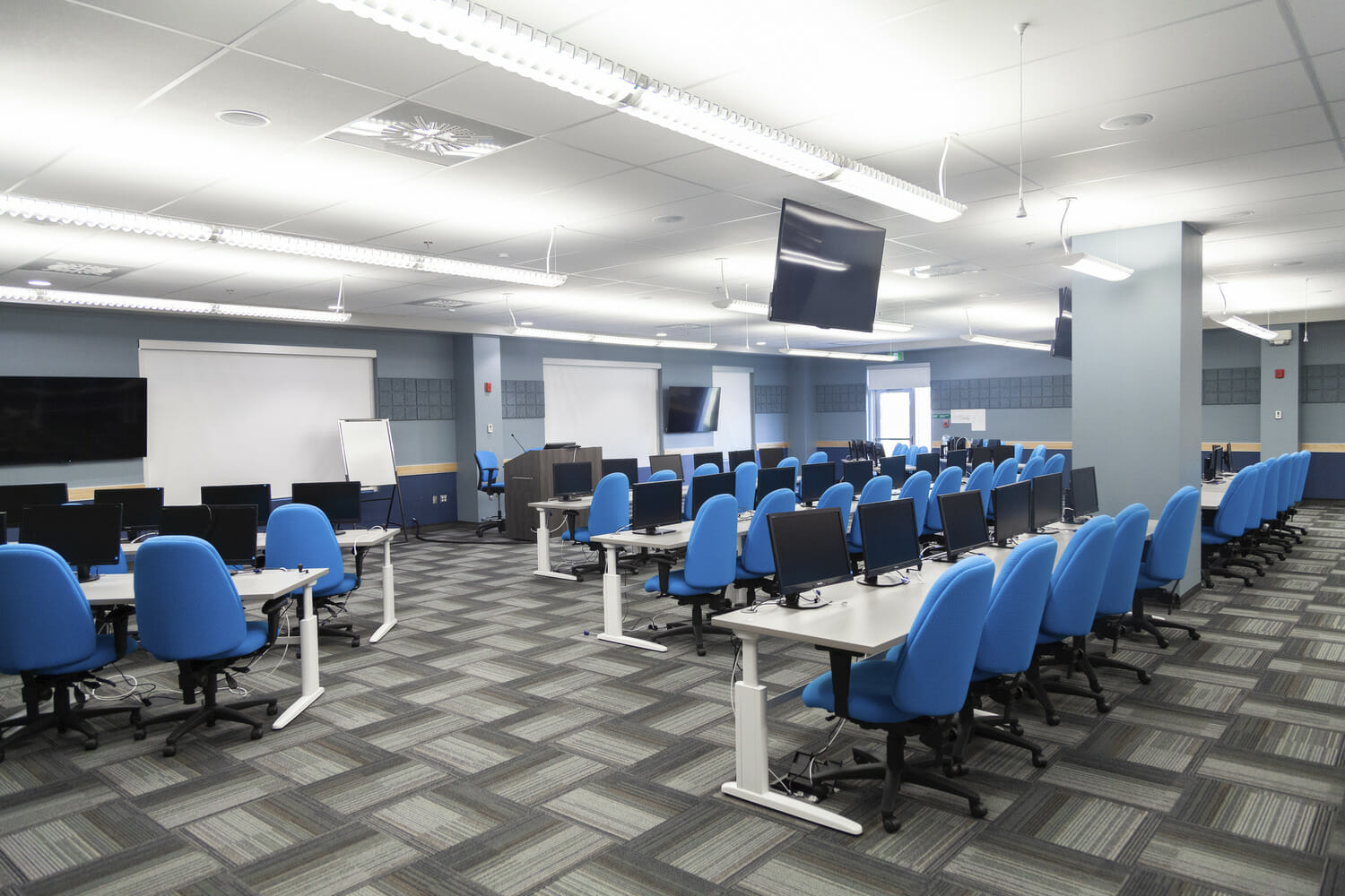 Une salle de classe avec des chaises bleues et des moniteurs.