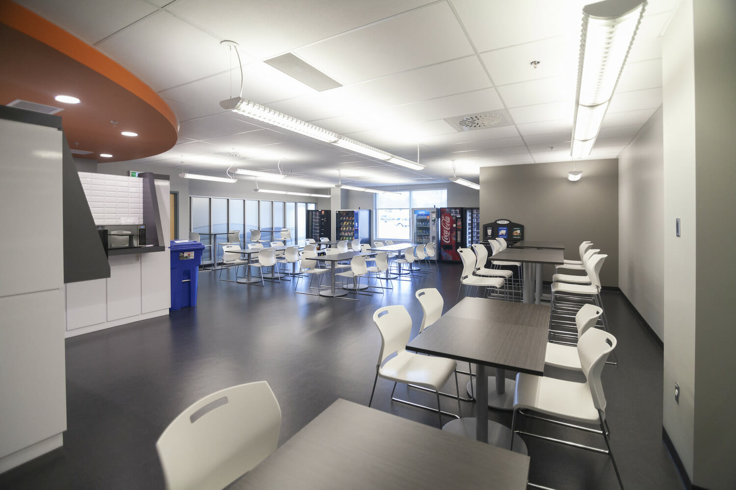 A cafeteria with white tables and chairs.