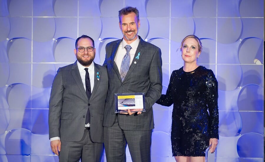 Three people standing next to each other holding an award.