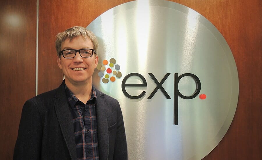 A man in glasses standing in front of the exp logo.
