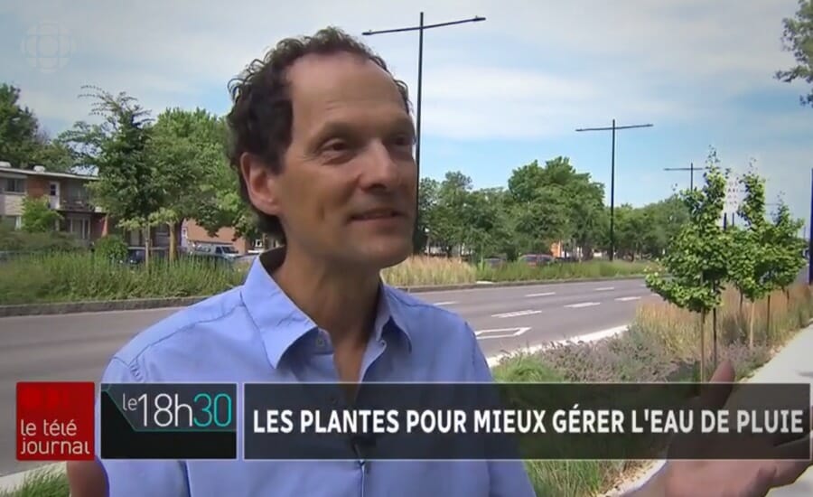 Un homme en chemise bleue se tient debout sur une rue, faisant un reportage sur le réaménagement de l'avenue Papineau.