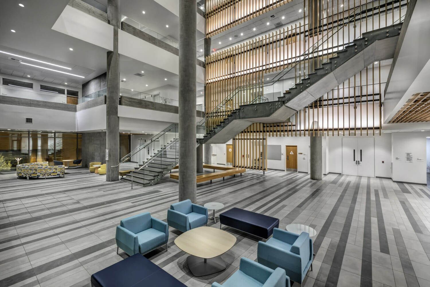 Le hall d’entrée d’un immeuble moderne avec des chaises et des escaliers bleus.