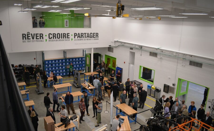 Un groupe de personnes se tient debout dans une grande salle lors de la cérémonie d'inauguration d'un nouveau studio de création à l'Université de Sherbrooke, célébrant l'innovation.