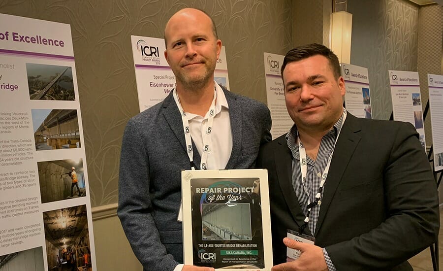 Two men standing in front of a poster with an award.