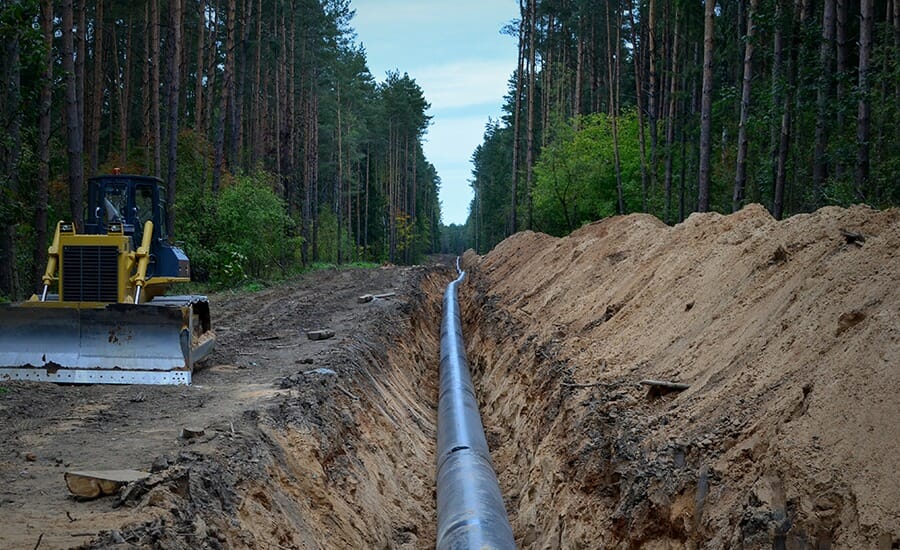 A bulldozer is working on a pipeline in the woods.