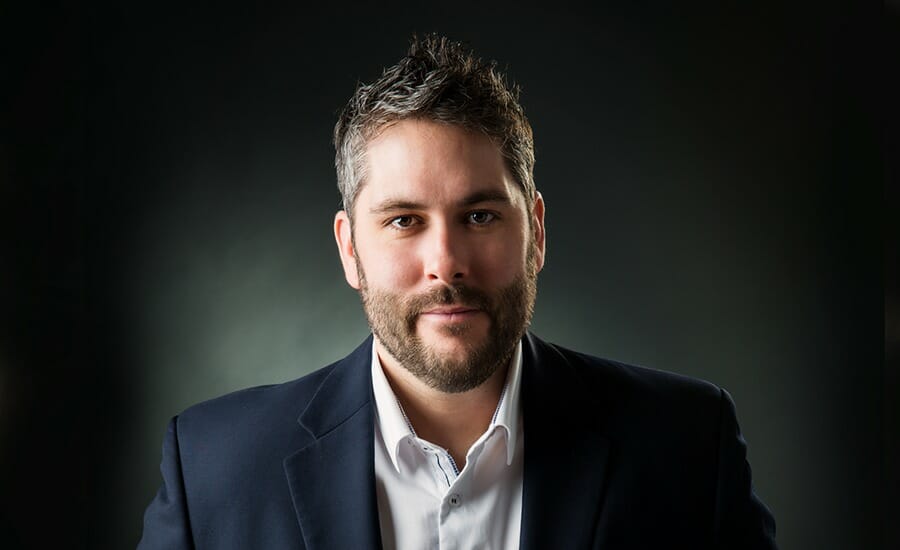 A bearded man in a suit poses for a photo.