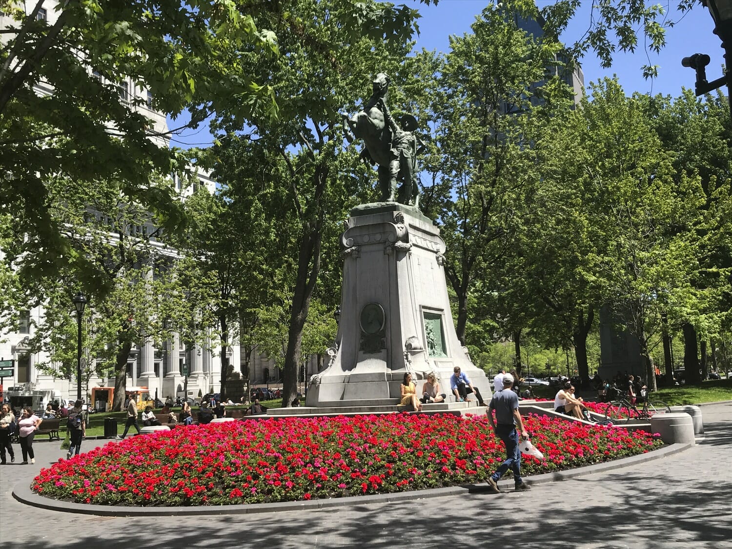 Une statue d'homme dans un parc entouré de fleurs rouges.