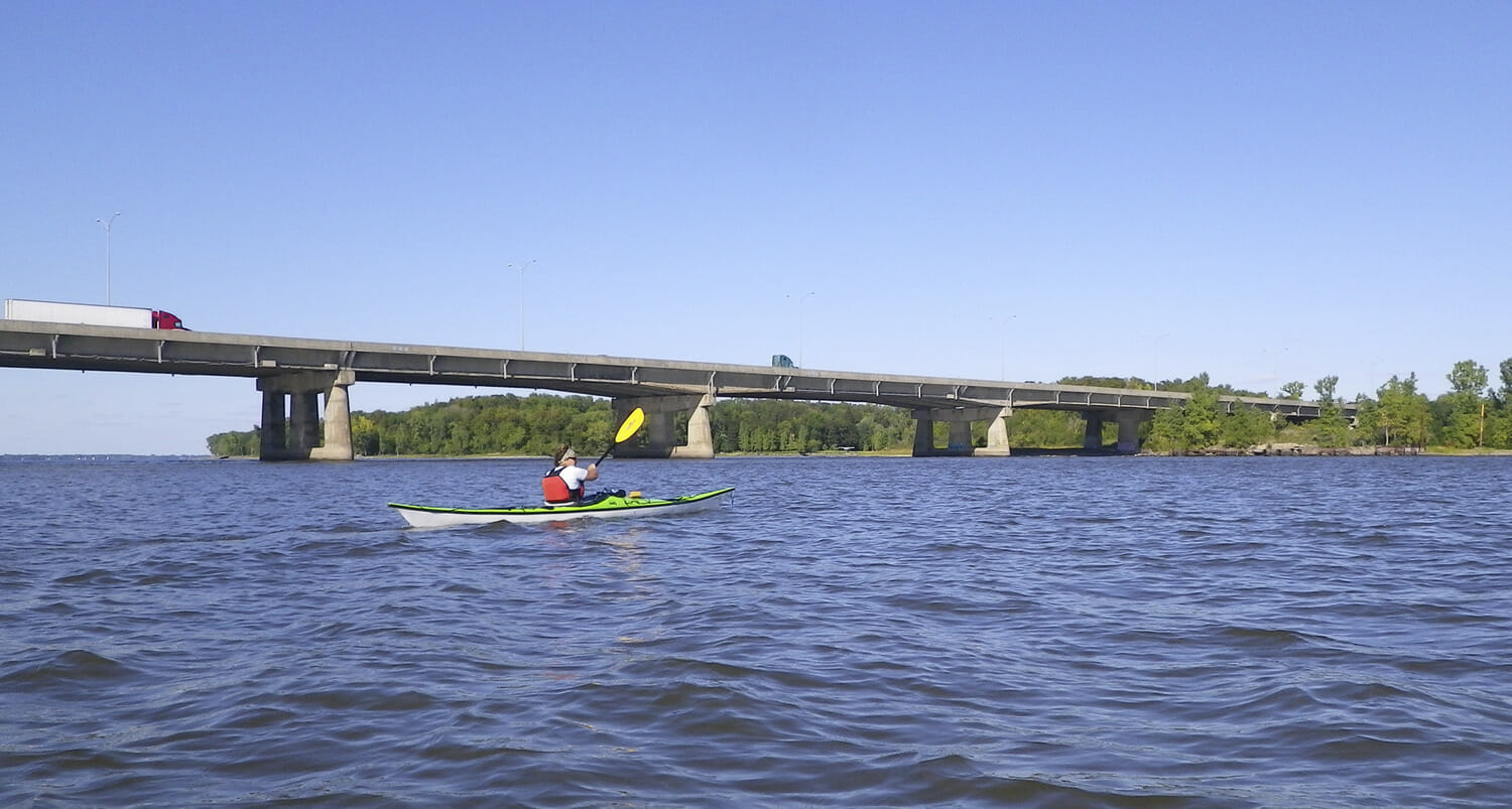 A person is paddling a kayak under a bridge.