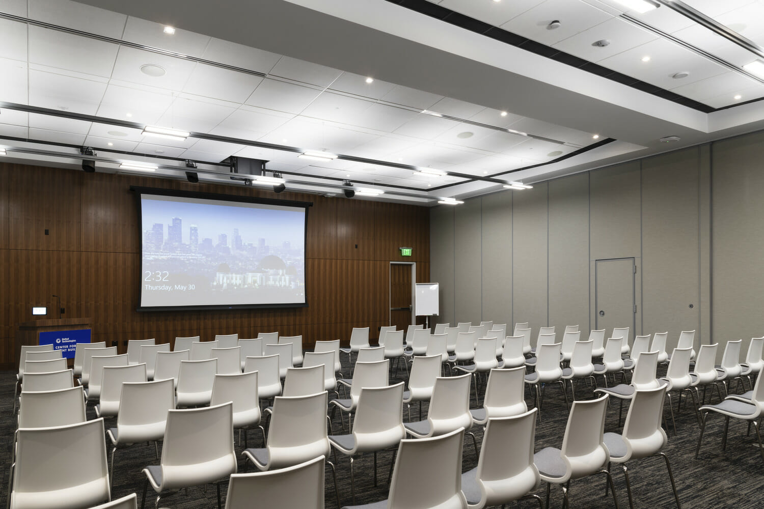 Une salle de conférence avec des chaises blanches et un écran de projection.