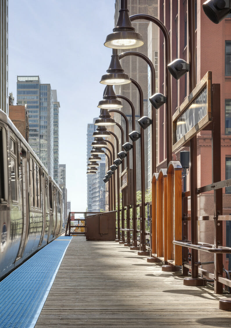 A train is parked on a platform in front of tall buildings.