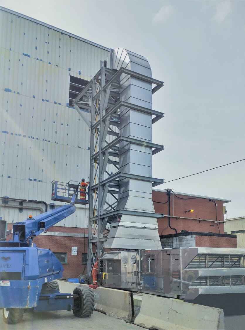 A crane lifts a large metal structure in front of a building.