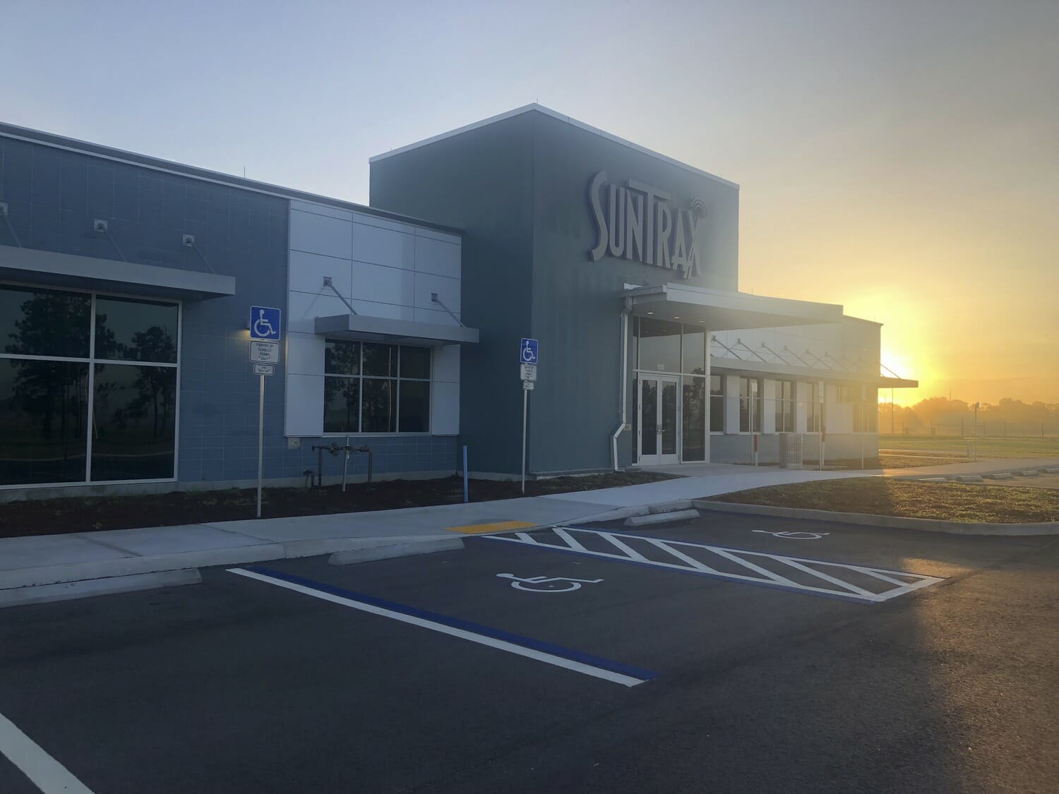 A building with a parking lot and a sun setting behind it.