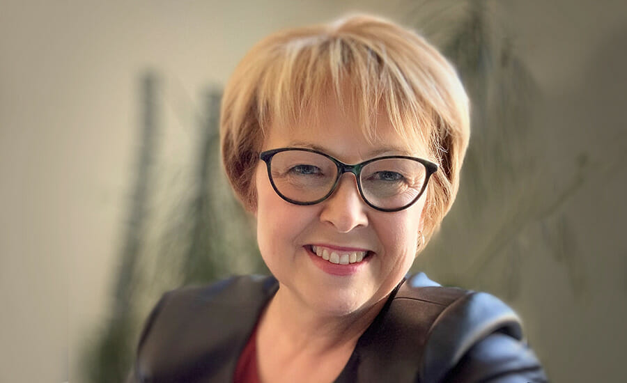 Une femme avec des lunettes souriant devant la caméra.