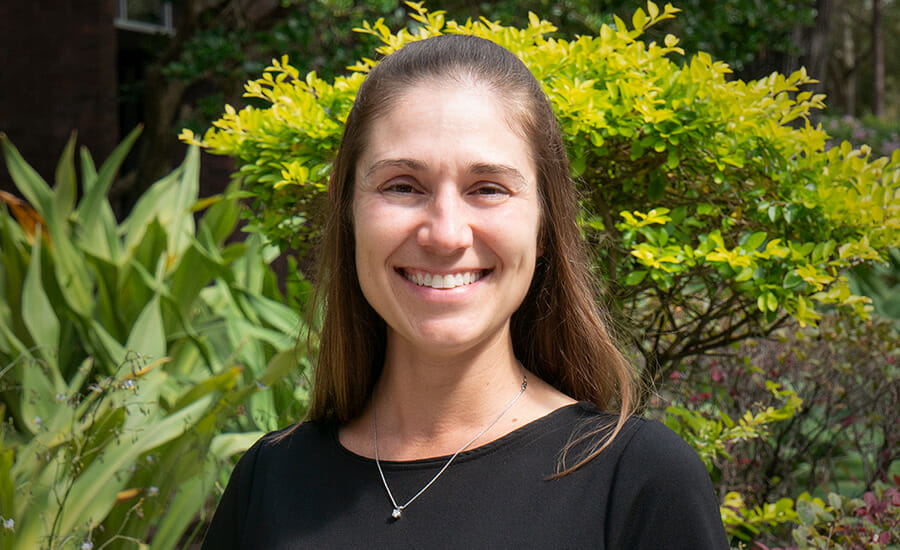 A woman smiling in front of bushes.