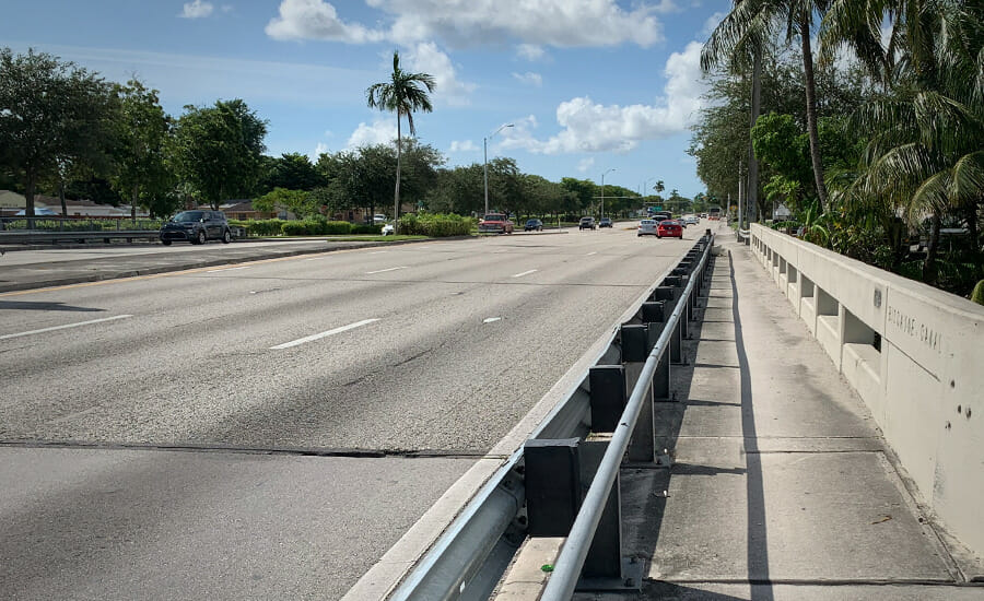 A highway with a concrete barrier and palm trees.