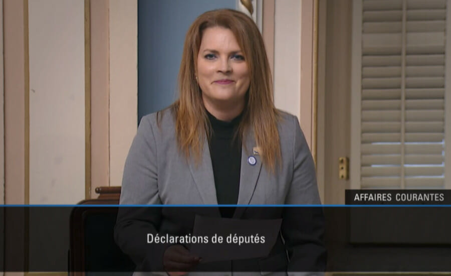 Une femme en costume est assise devant une télévision.