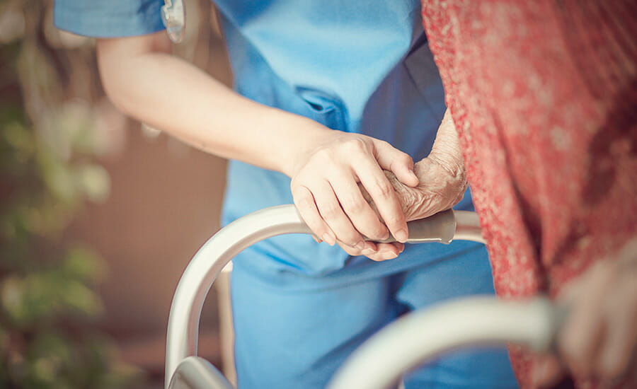 Une infirmière tient la main d'une femme âgée sur un déambulateur.