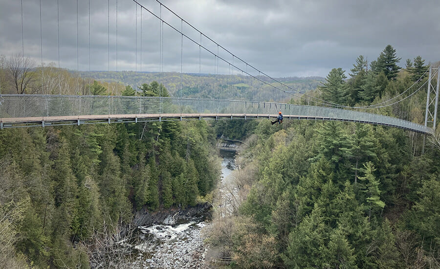 Une personne se tient debout sur un pont suspendu au-dessus d’une rivière.