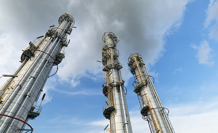 A group of oil refinery towers against a cloudy sky.