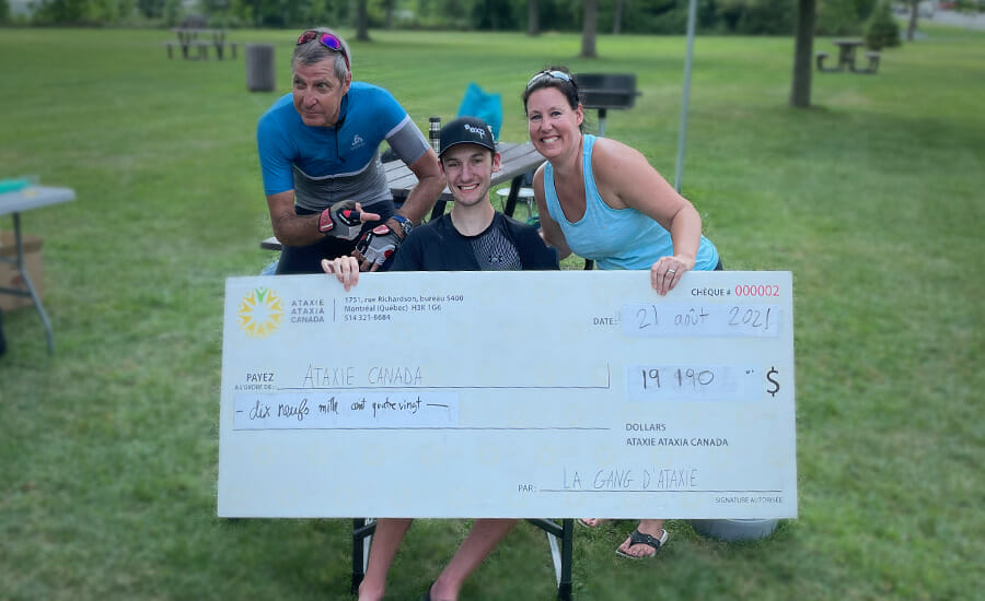 Three people posing with a large check in a park.