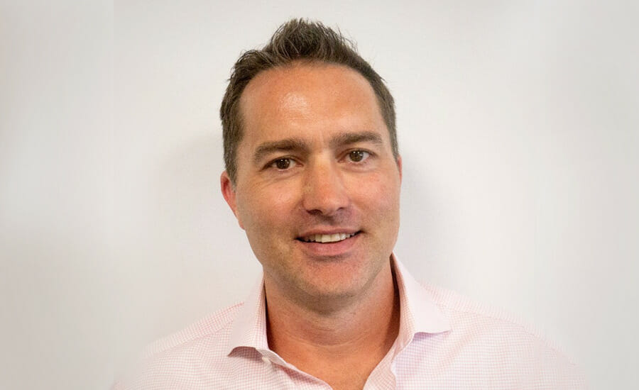 A man in a pink shirt smiling in front of a white wall.