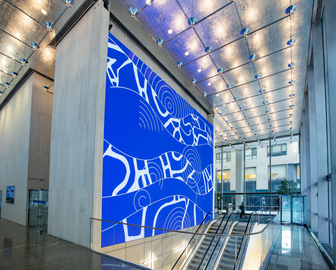 A large blue wall in a building with escalators.