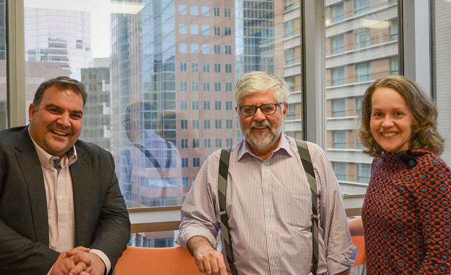 Trois personnes debout devant une fenêtre dans un bureau.