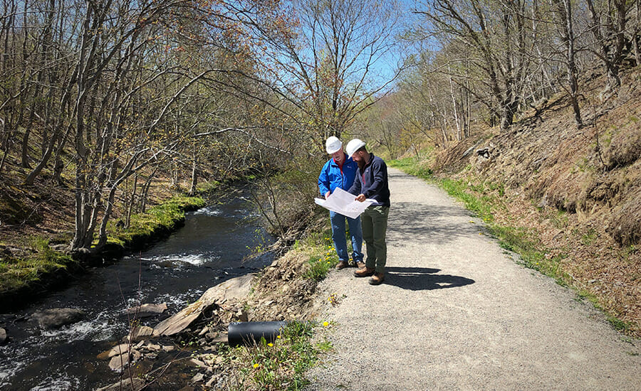 Two people standing on a path near a river.