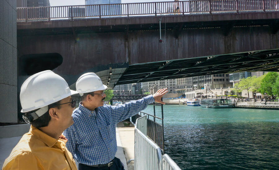 Two men in hard hats standing on a bridge.