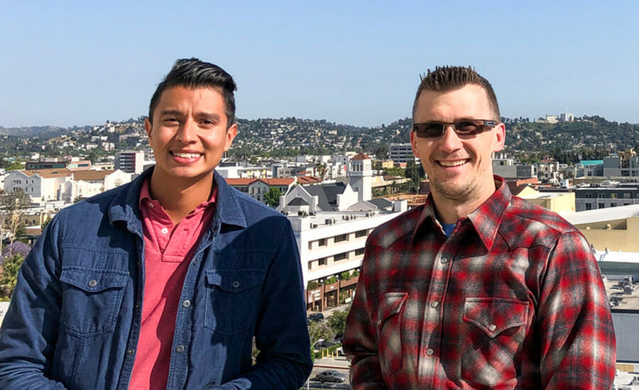 Two men standing next to each other in front of a city.