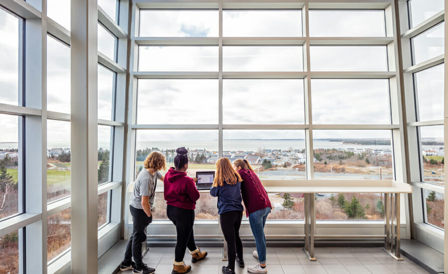 Quatre étudiants regardant par une grande fenêtre.