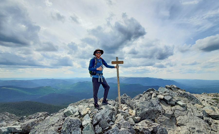 Un homme debout au sommet d’une montagne avec une pancarte.