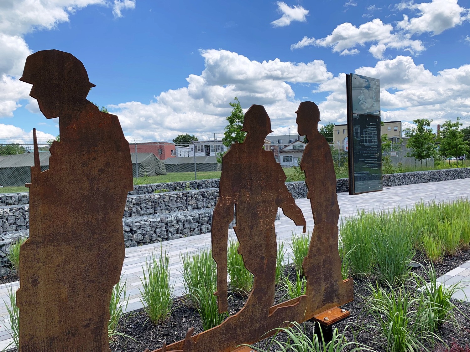 A metal sculpture of soldiers in front of a grassy area.