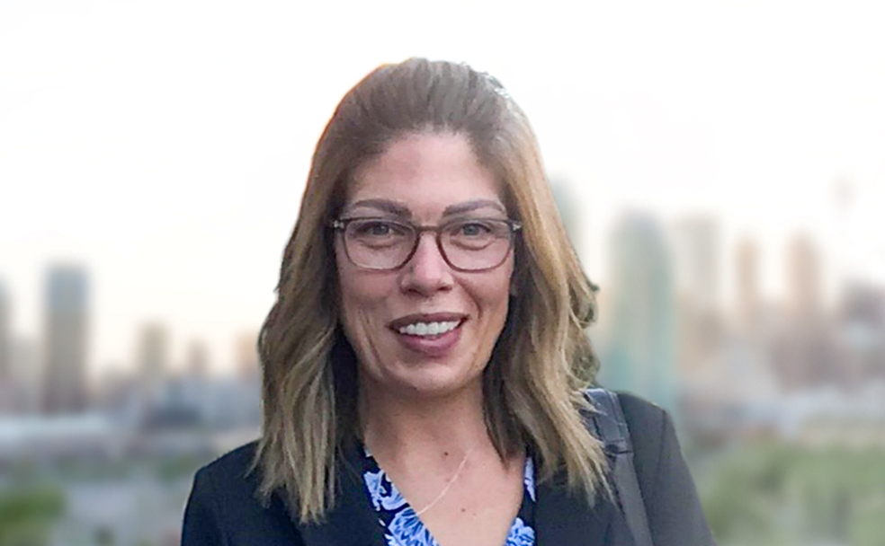 A woman in glasses smiling in front of a city skyline.