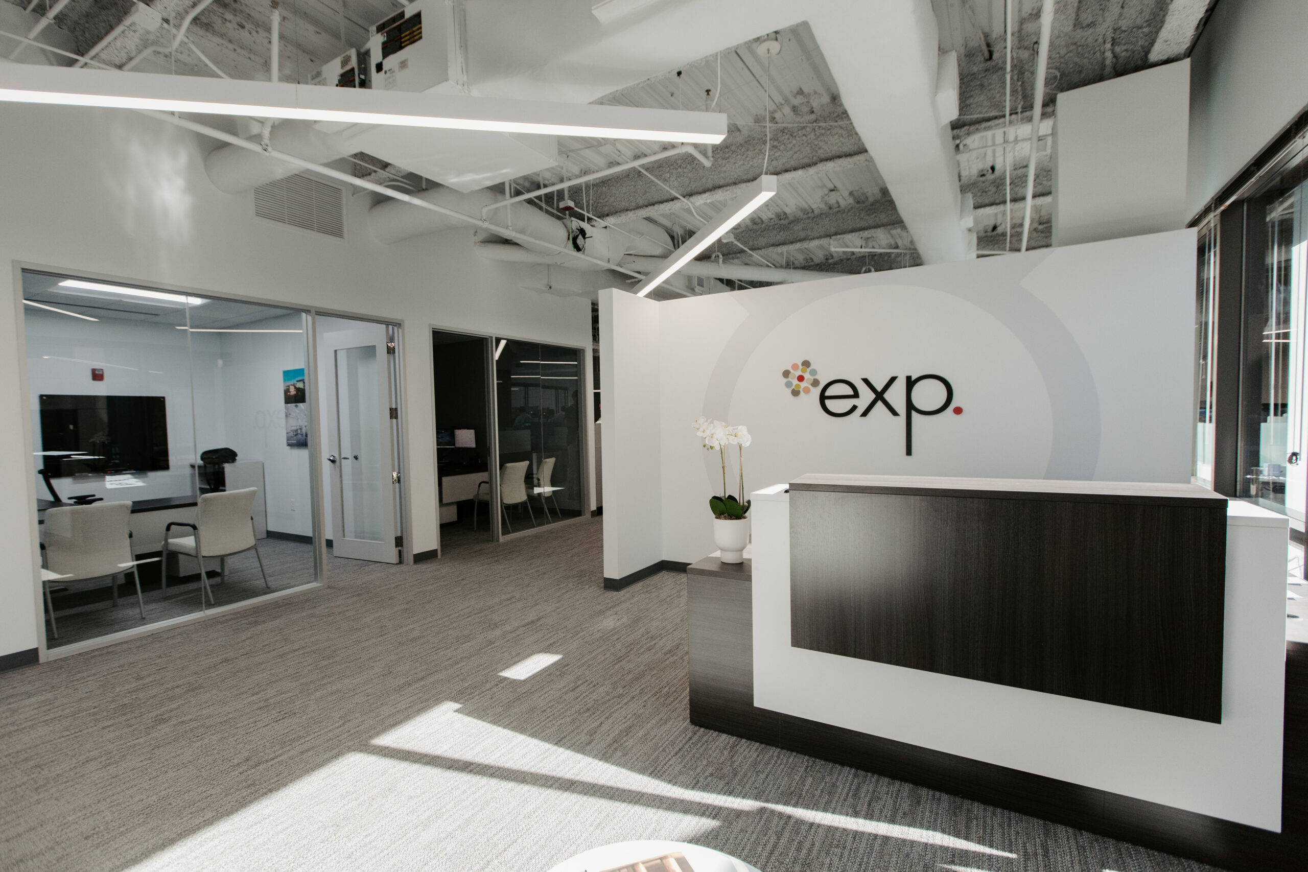Modern office lobby with a reception desk featuring the company logo 'exp' and a clean, minimalist design.