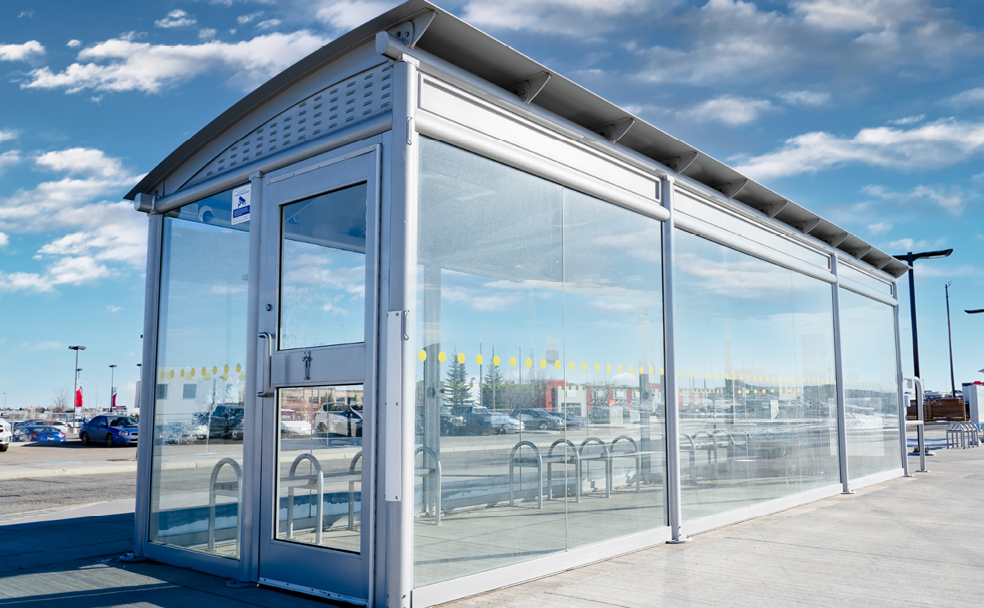 A glass bus stop with a blue sky.